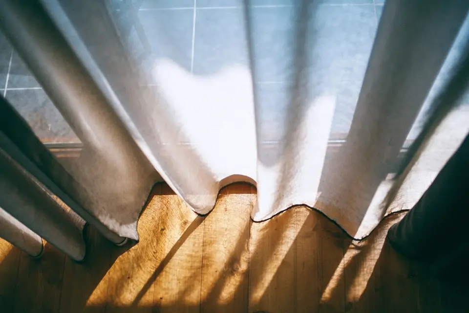 Low sunlight passing through linen curtains and casting stripes on a wooden floor
