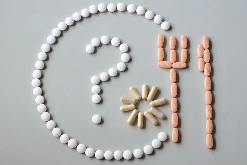 Tablets and capsules arranged as a question mark on a plate beside a fork, seen from above