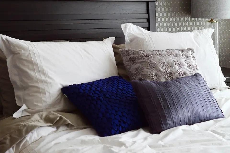 A made bed with white and navy blue pillows against a dark headboard