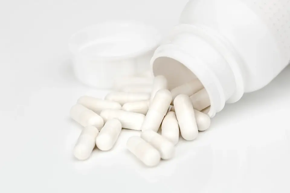 White capsules spilling out of an unlabelled white bottle
