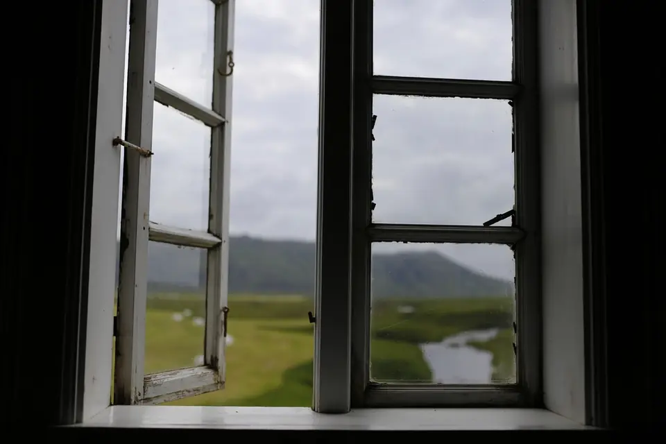 An open wooden casement window looking out over green fields