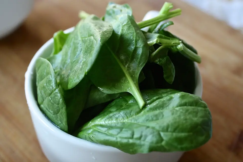 Fresh spinach leaves in a white bowl on a wooden table