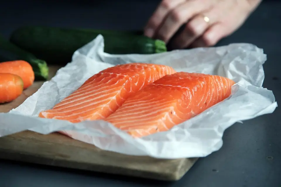 Two raw salmon fillets on baking paper on a wooden board