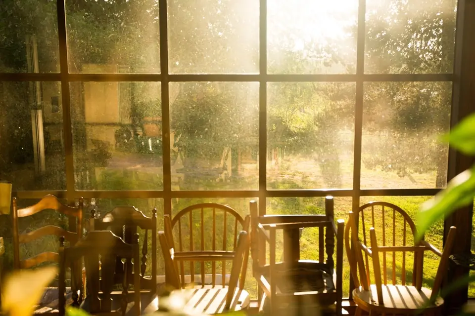 Early sunlight streaming through a large window onto wooden chairs and tables