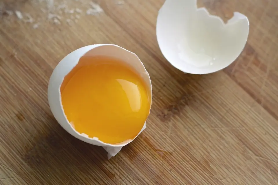 A cracked egg with its yolk in the shell on a wooden board