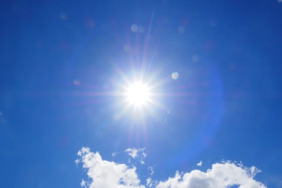 A bright sun in a deep blue sky above a few white clouds